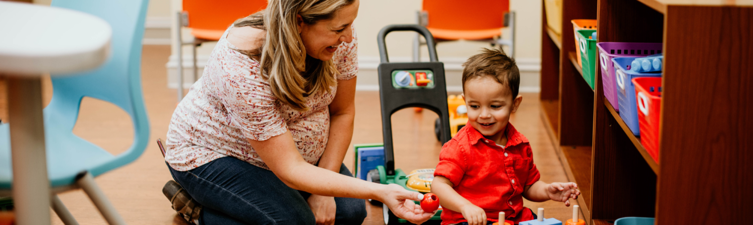 young woman handing her small child a toy as they play in the Watson Institute's Austin's Playroom