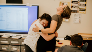 happy student hugs behavior technician staff member while they laugh in the classroom - Watson Institute