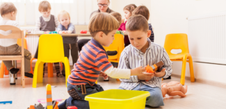 preschool-age students pictured playing together with other students playing nicely in the background in a classroom setting - Watson Institute