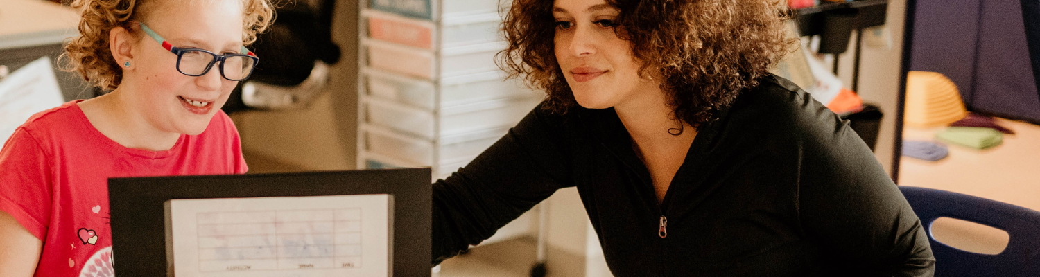 behavior technician is helping a student navigate something on a laptop - Watson Institute