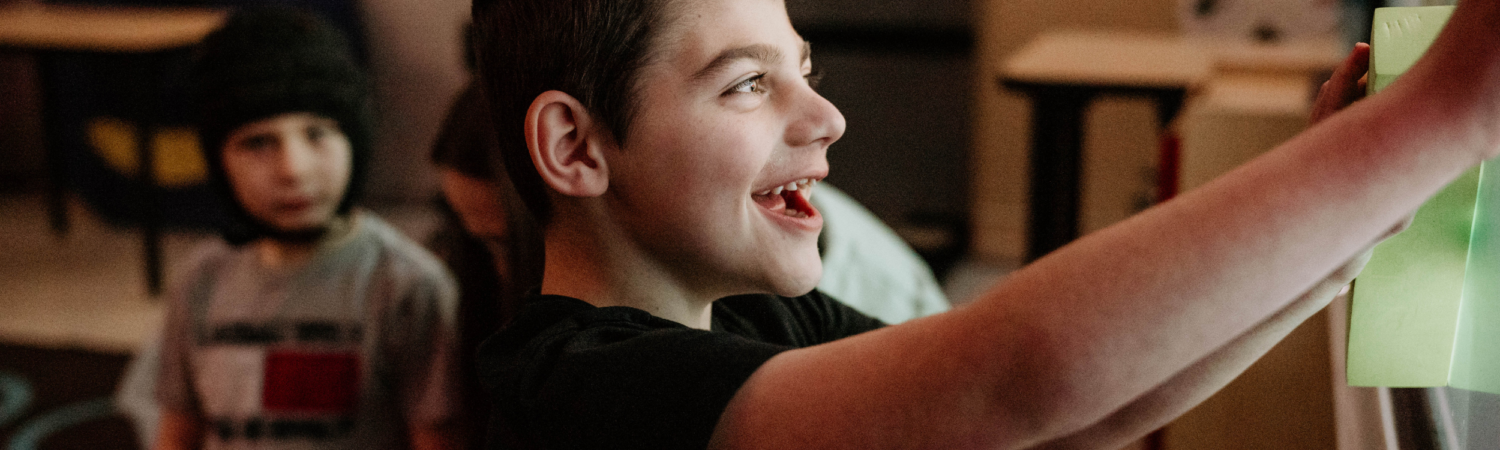 young boy with special needs shown smiling at the classroom smart board