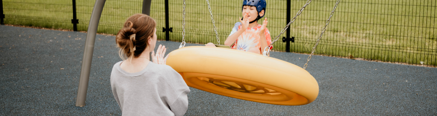 young boy with special needs on an adaptive swing outside with his teacher