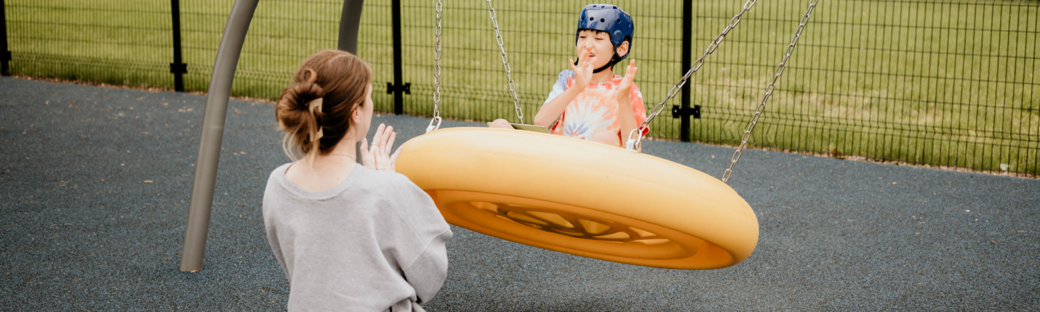 young boy with special needs on an adaptive swing outside with his teacher