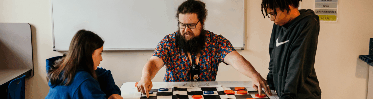 special education teacher facilitating a game of checkers with two autistic students in the classroom - Watson Institute