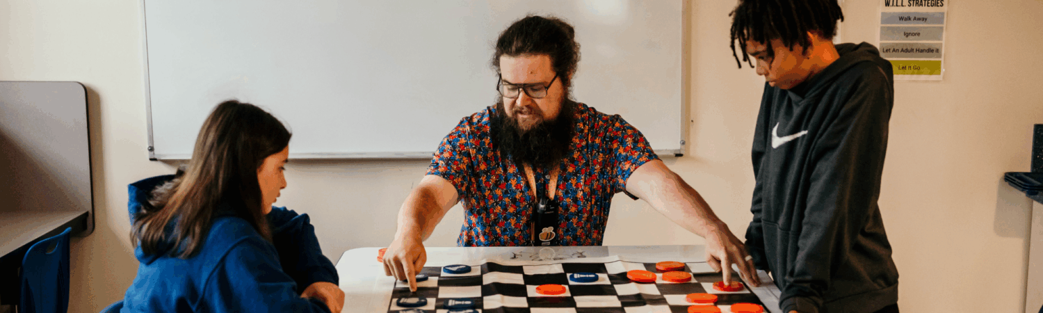 special education teacher pictured facilitating a game of checkers with two autistic students in the classroom