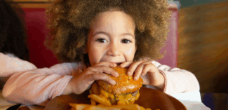 young child eating a burger - social skills to act appropriately in a restaurant