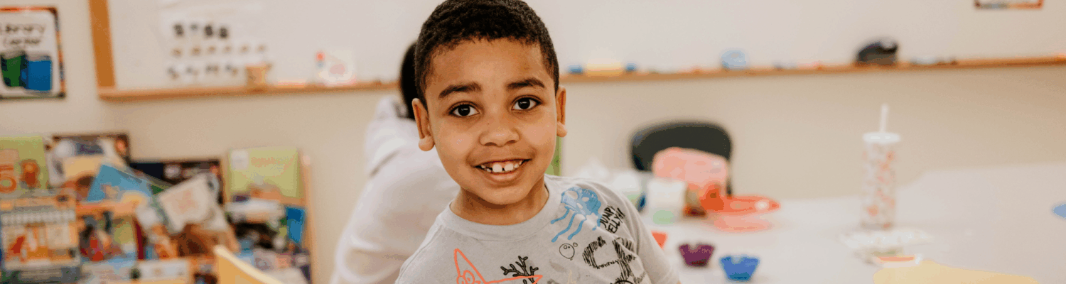 young boy smiling in his classroom at Friendship Academy - Watson Institute