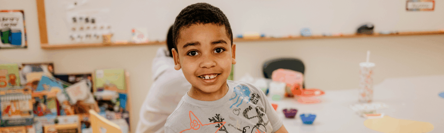 young boy smiling in his classroom at Friendship Academy - Watson Institute