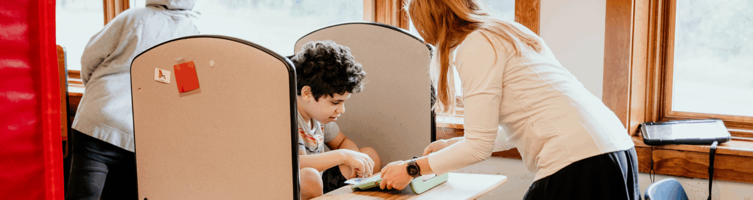special education teacher helping student with special needs at their desk in the classroom - Watson Institute