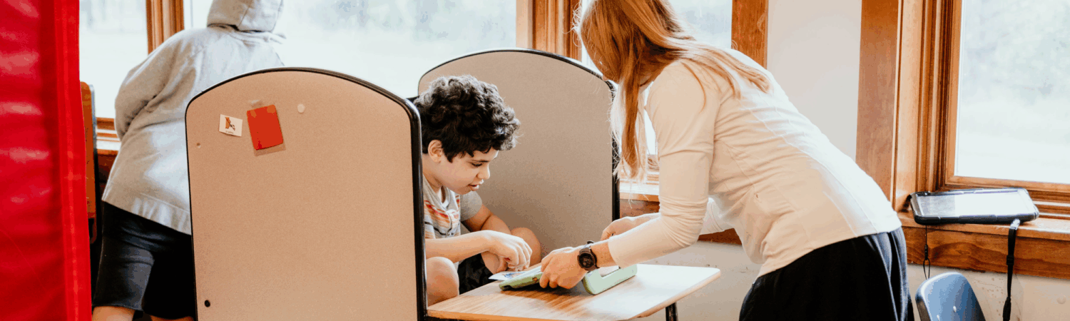 special education teacher helping student with special needs at their desk in the classroom - Watson Institute