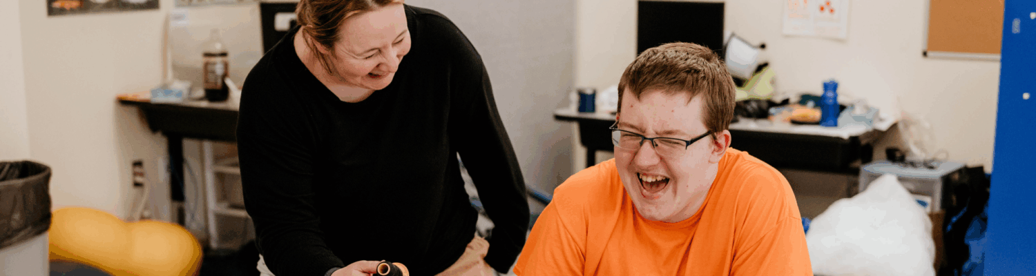 special education teacher laughing alongside their student with autism in the classroom - Watson Institute
