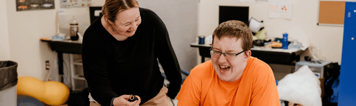 special education teacher laughing alongside their student with autism in the classroom - Watson Institute