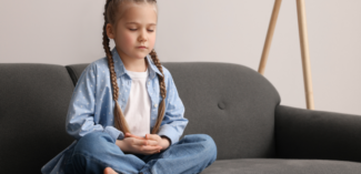 a young child is seated calmly with her eyes closed employing calming strategies - Watson Institute