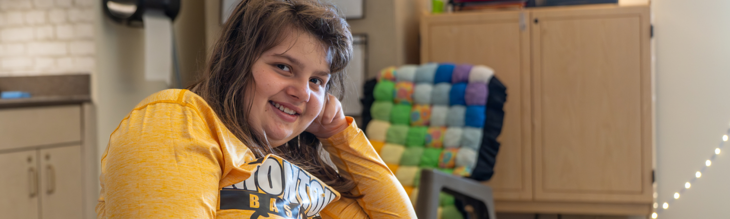 a student with special needs smiles while seated in their classroom - Watson Institute
