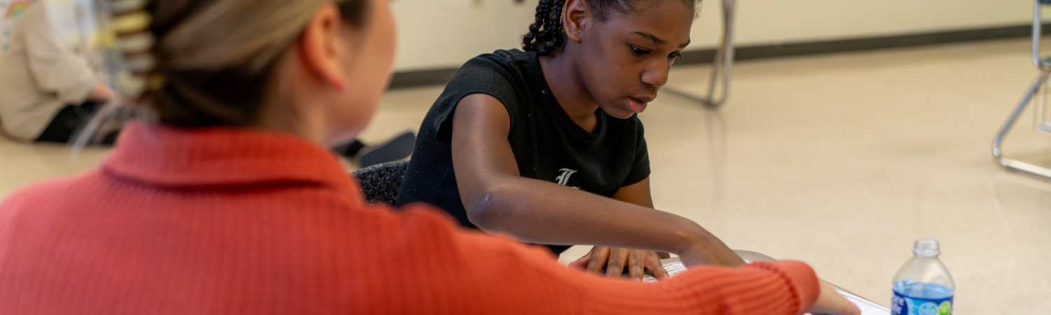special education teacher helps a student work through an assignment in the classroom - Watson Institute