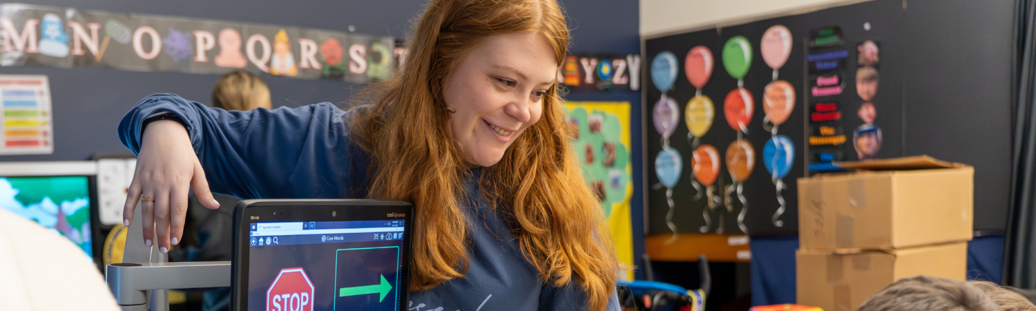 a speech language pathologist helps a student with disabilities participate in morning meeting using an adapted communication device - Watson Institute