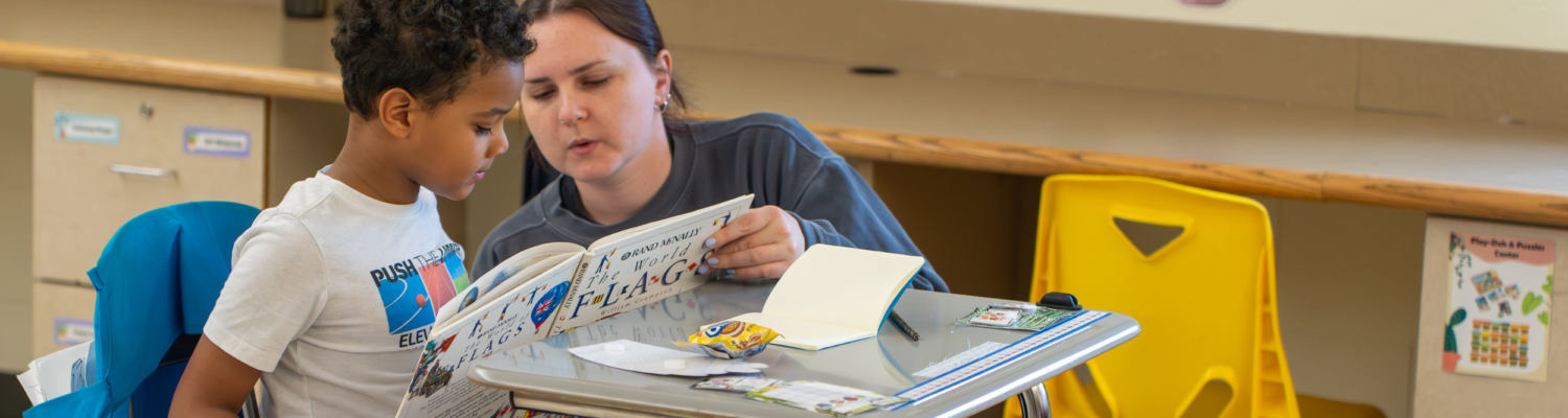 a special education teacher helps a young student read a book in an emotional support classroom - Watson Institute