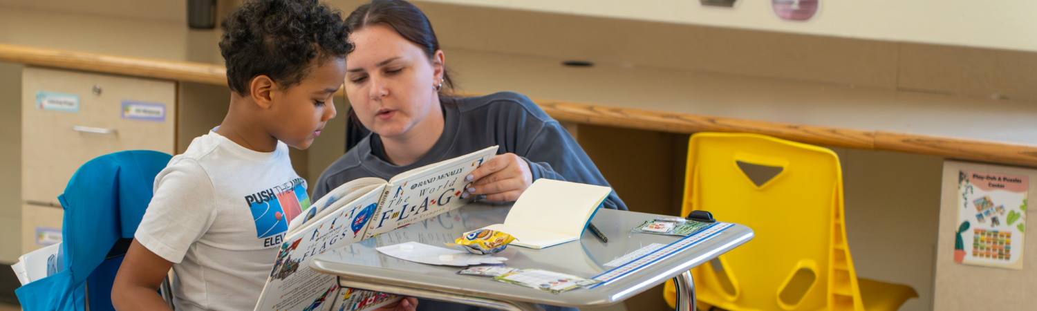a special education teacher helps a young student read a book in an emotional support classroom - Watson Institute