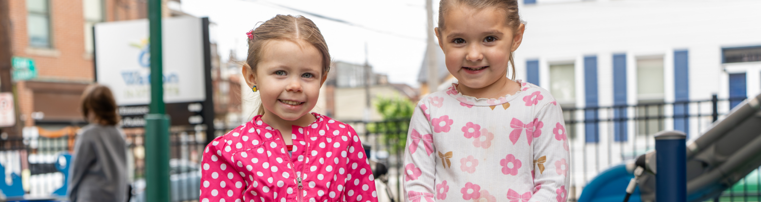 two preschool students smile on the playground outside of their inclusive preschool program - Watson Institute