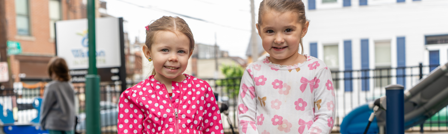 two preschool students smile on the playground outside of their inclusive preschool program - Watson Institute