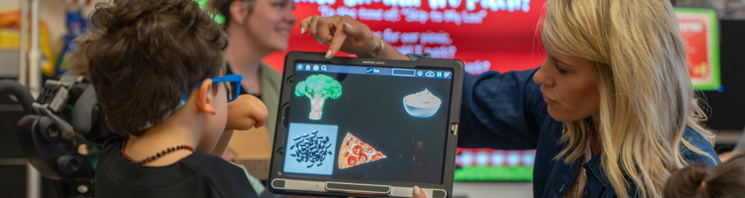 a special education teacher helps a student with a visual impairment locate a visual icon on his tablet in the classroom during a lesson - Watson Institute