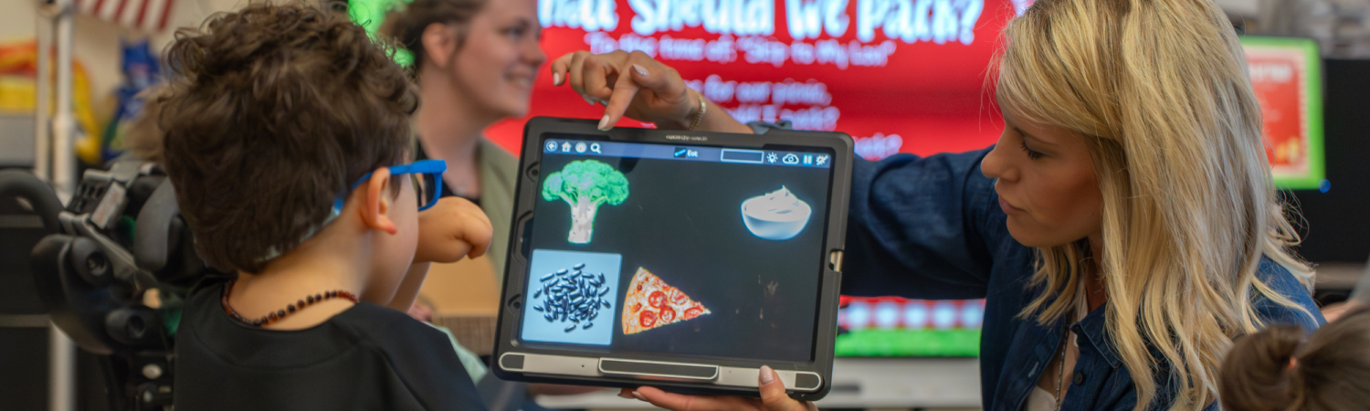 a special education teacher helps a student with a visual impairment locate a visual icon on his tablet in the classroom during a lesson - Watson Institute