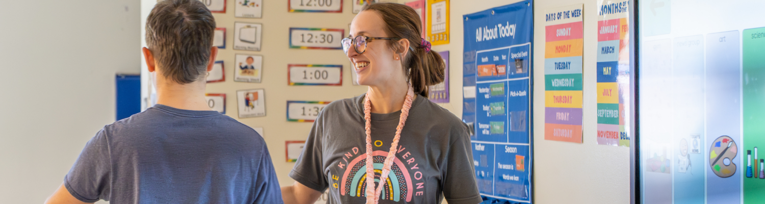 a special education teacher smiles at a student with special needs as he leaves the SmartBoard during morning meeting - Watson Institute