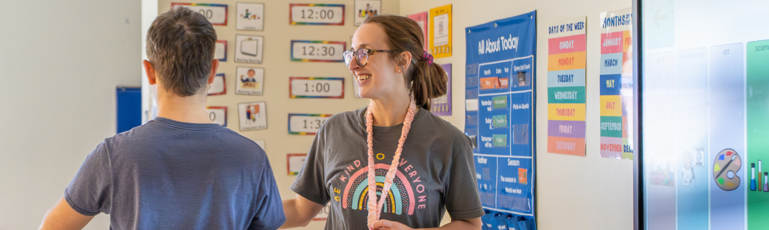 a special education teacher smiles at a student with special needs as he leaves the SmartBoard during morning meeting - Watson Institute