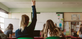 a student has their hand raised during class to ask a question - Watson Institute