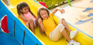 Two children going down a playground slide close together sharing space in close proximity - Watson Institute