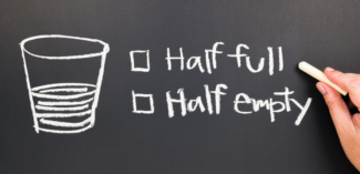 image depicts a cup drawn on a chalkboard showing it half filled with liquid and two options to check off; either half full or half empty, indicating differing perspectives - Watson Institute