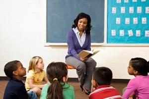 teacher seated in front of class of young children sitting around her on the floor