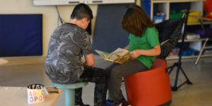 two students sit together reading a book in a classroom