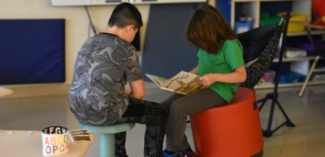 two students sit together reading a book in a classroom