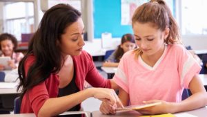 young female educator reviewing school work with a young female student at her desk in a classroom