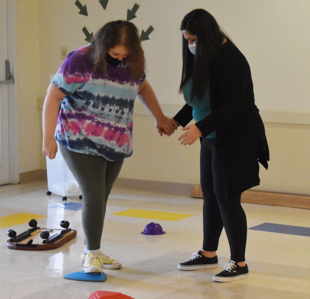 occupational therapist holding the hand of a student while they practice balancing