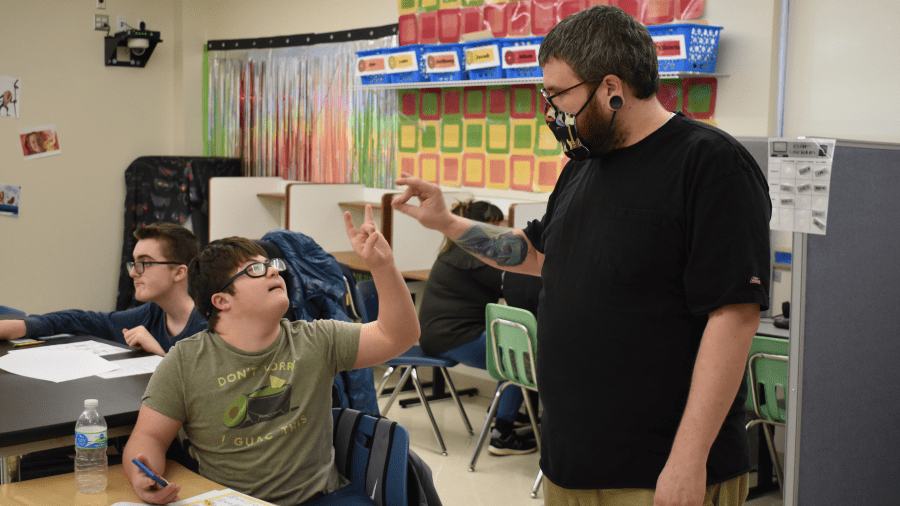 Behavior Technician staff member does a hand shake sign with a student with special needs in a classroom setting.