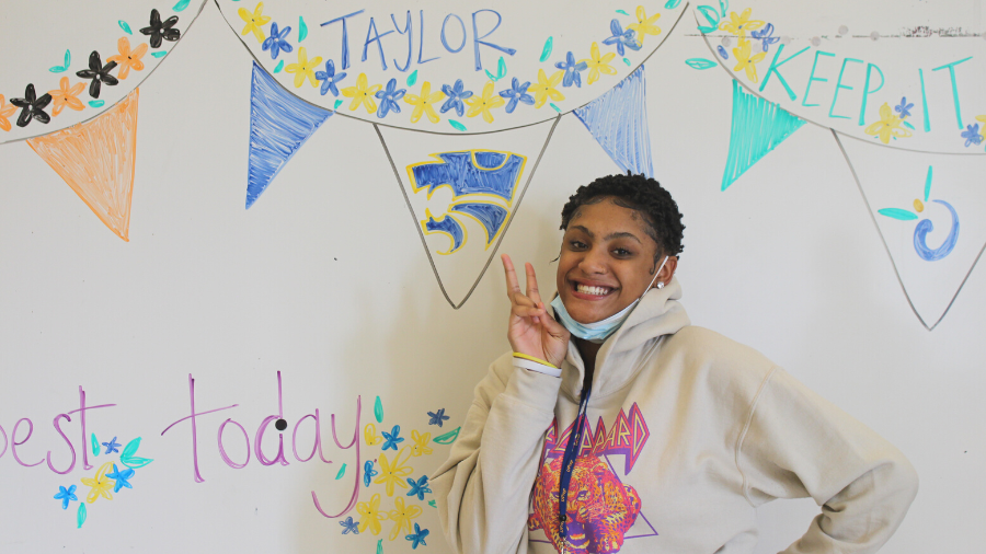 Student who is transitioning from Friendship to their home school district is posed in front of a dry erase board with her name pictured at a celebration for her accomplishment.