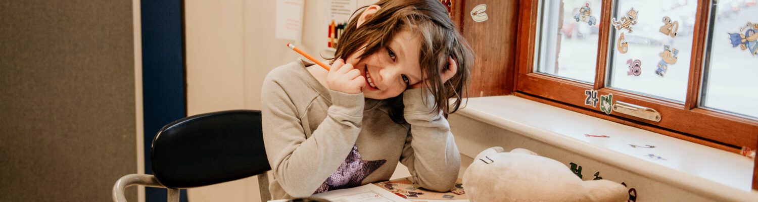 Student smiling shyly at the camera while working at her desk.