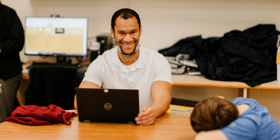 Classroom therapist seated at a table with laptop smiling at the camera.