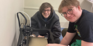 two autistic students posing with a 3D printer in their school's Makerspace