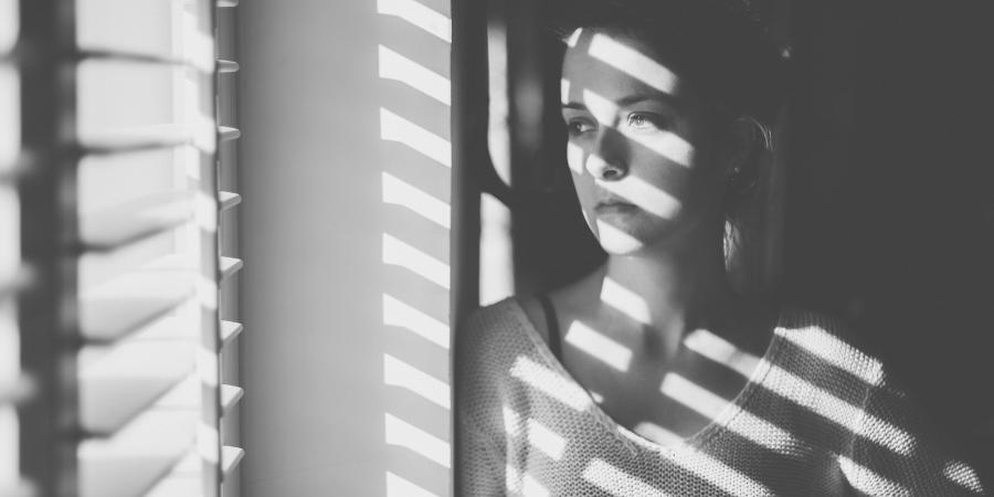 a young woman looks out of the window through blinds. photo is in black and white