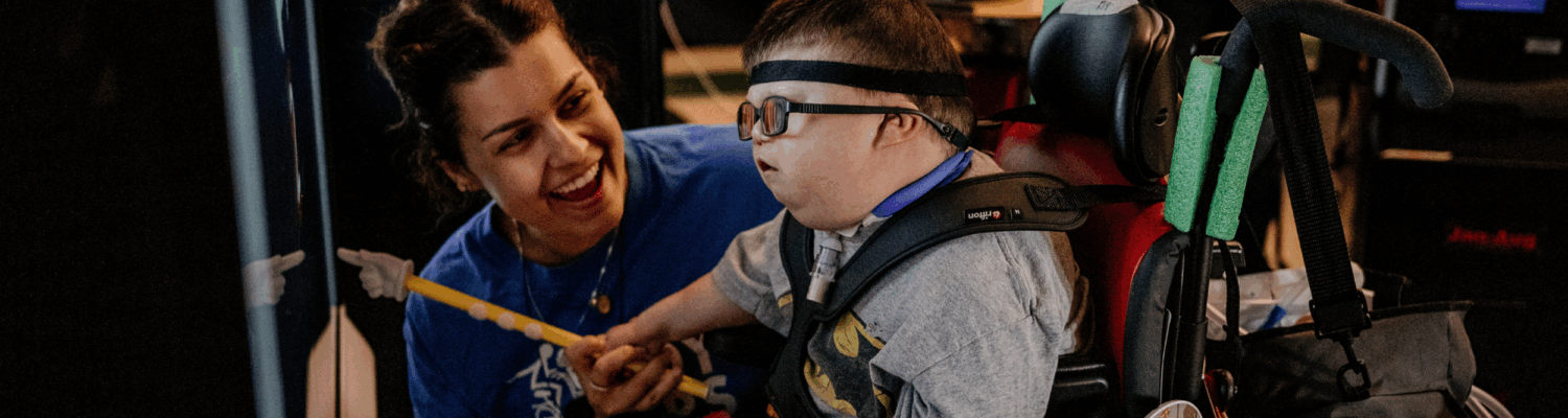 special education teacher helping young student with physical disabilities in the classroom - Watson Institute