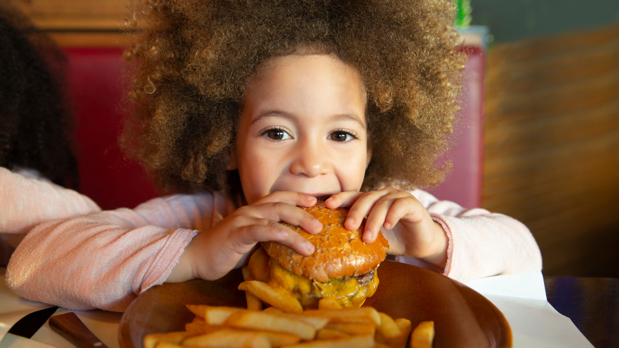 young child eating a burger - social skills to act appropriately in a restaurant