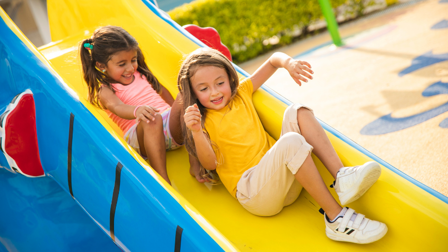 Two children going down a playground slide close together sharing space in close proximity - Watson Institute
