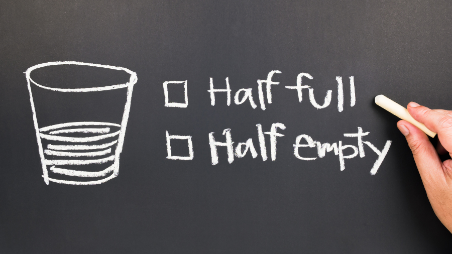 image depicts a cup drawn on a chalkboard showing it half filled with liquid and two options to check off; either half full or half empty, indicating differing perspectives - Watson Institute